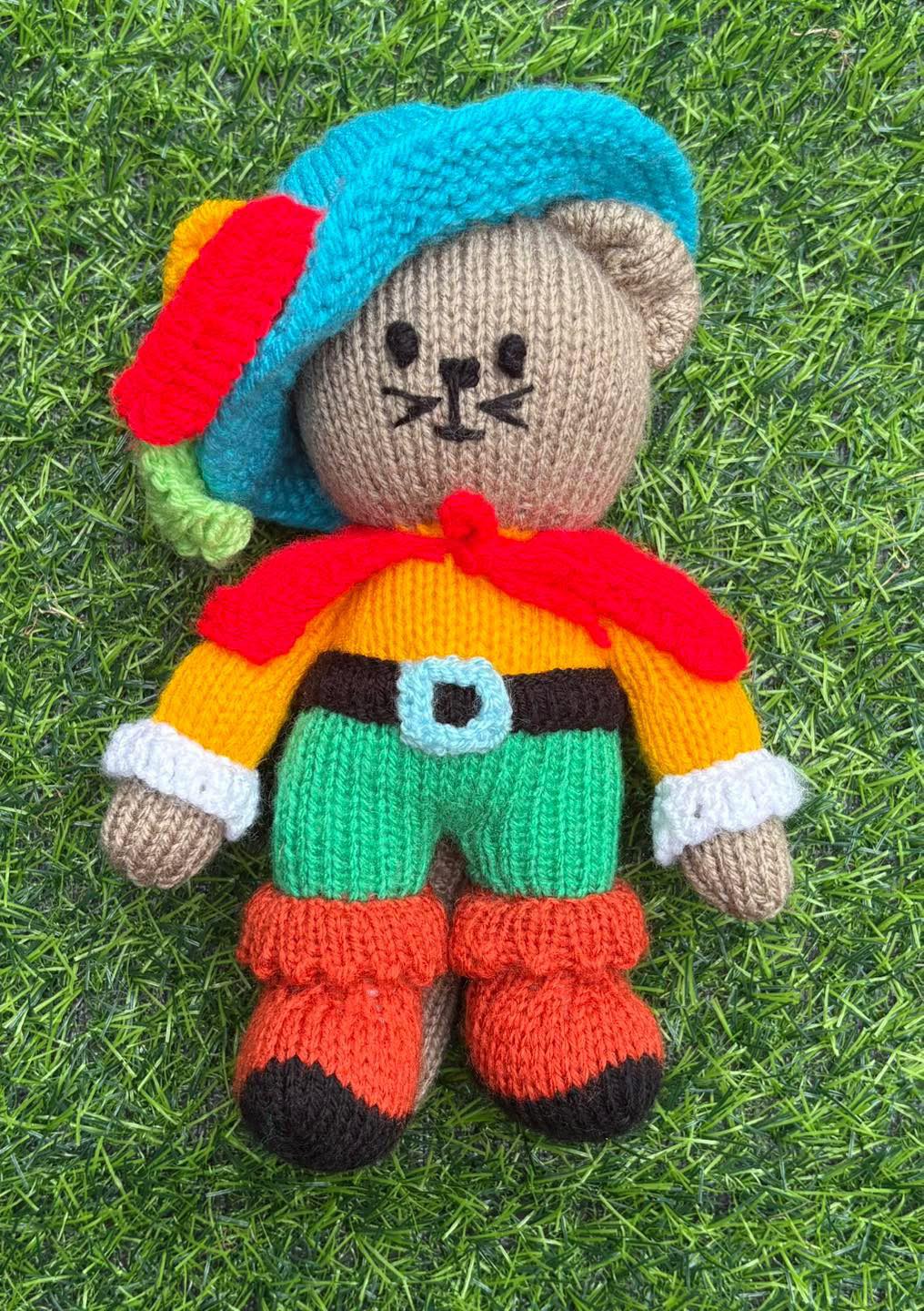 Christmas Craft Sale 2025. Item 79. “Fear me, if you dare!” Beautifully knitted Puss in Boots! He’d love to come and guard your honour and potentially save your life! We love him! Measures approx 21cm tall. So cuddly!